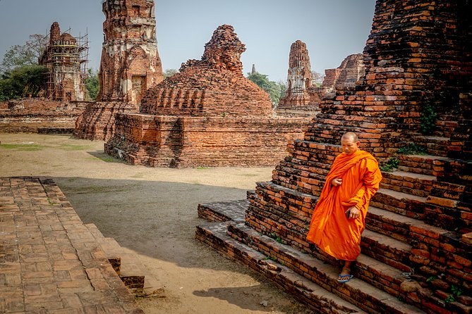 A monk in an orange robe walking between the brick ruins of the historical park