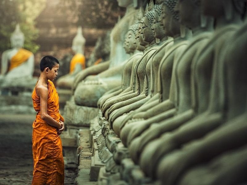 A monk walking past a long row of seated Buddha statues