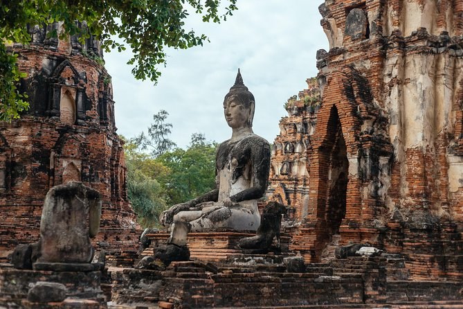 A weathered seated Buddha in front of a ruined brick prang